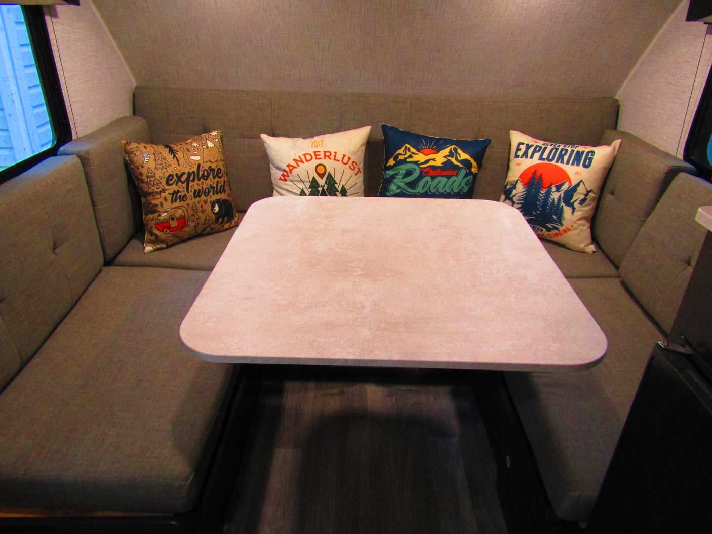 This RV rental dinette features U-shaped seating, a central table, and adventure-themed throw pillows. A cozy camper interior.