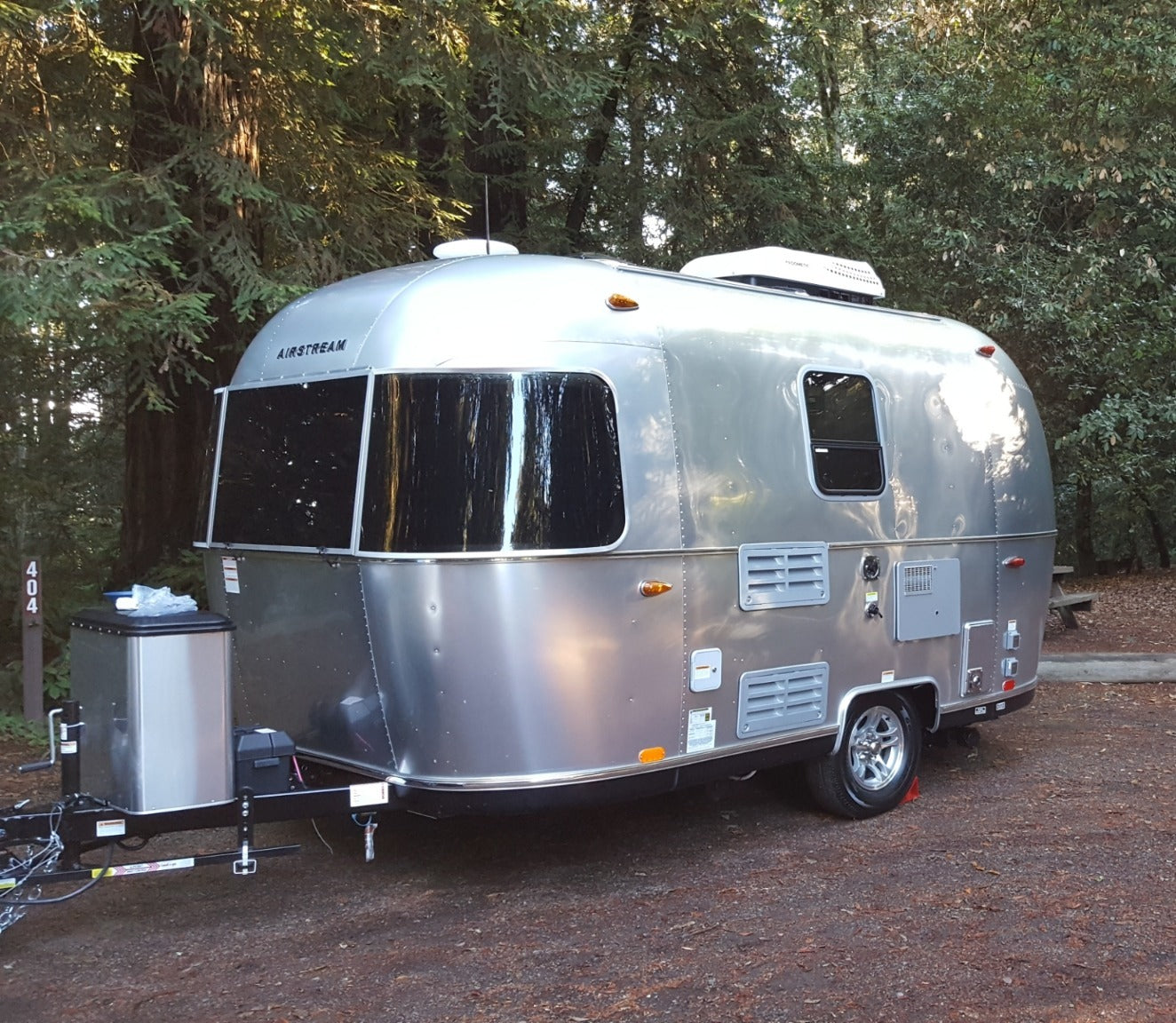 A classic silver Airstream travel trailer, perfect for an rv rental, is parked in a tranquil, wooded campground.