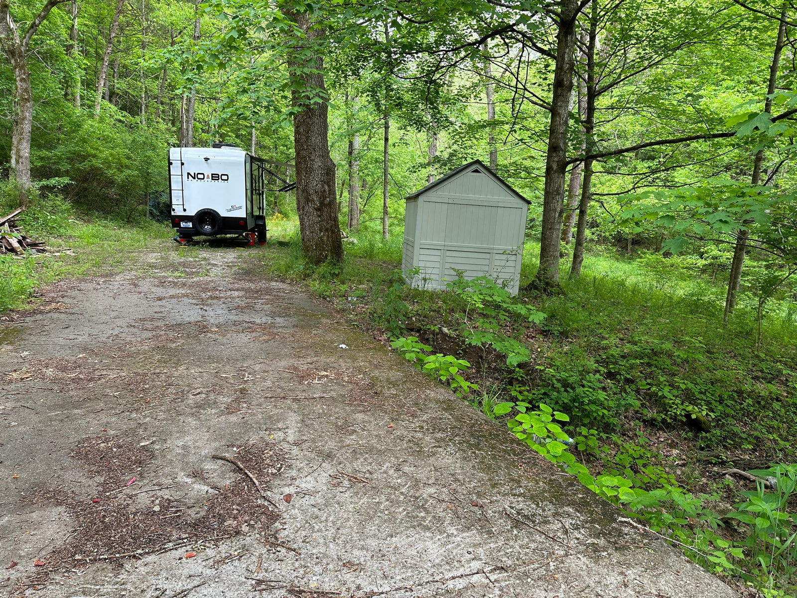 NOBO **RV rental** parked on a forest clearing beside a shed, with a paved approach. Ideal for a nature escape.