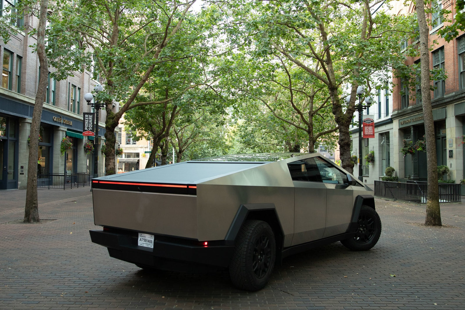 A grey Tesla Cybertruck on an urban brick street. Its unique design could suit an rv rental adventure. Trees & buildings.