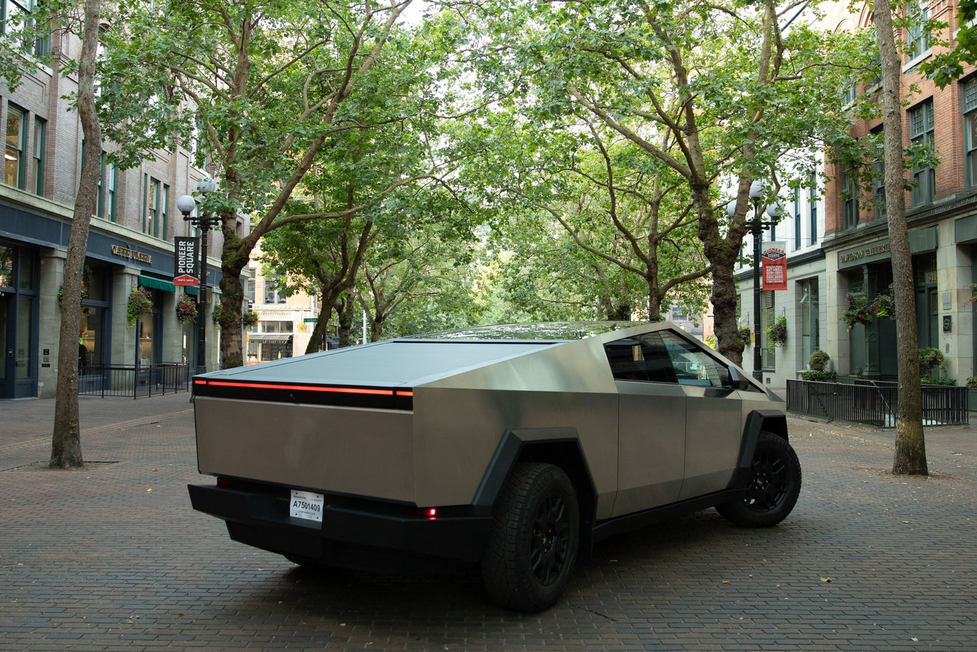 A grey Tesla Cybertruck on an urban brick street. Its unique design could suit an rv rental adventure. Trees & buildings.