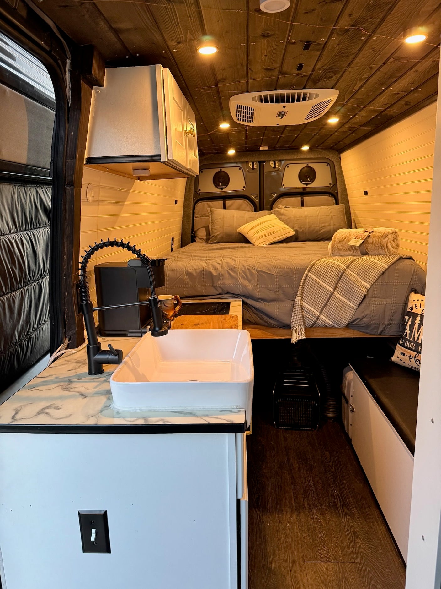Cozy RV rental interior with bed, kitchen, and wood ceiling. Perfect for compact living on the road.
