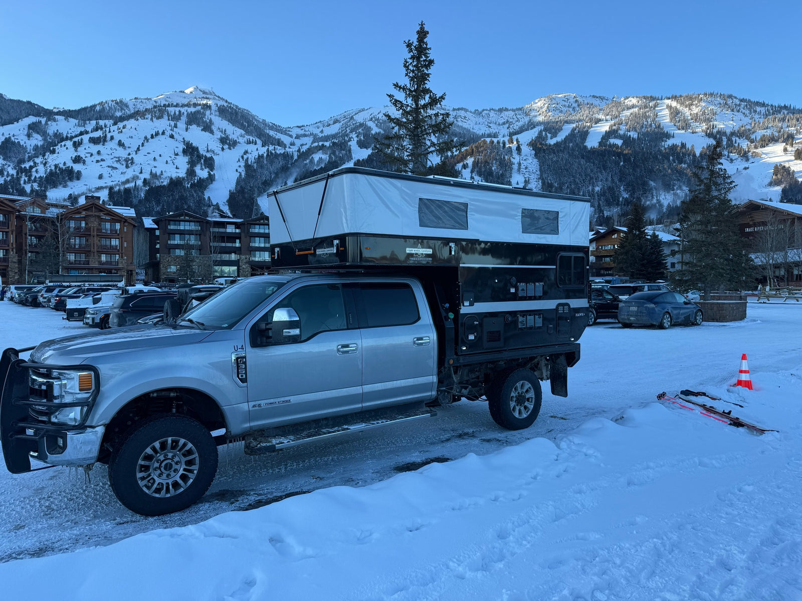 RV rental: Silver Ford F-250 with a Four Wheel Campers Hawk+ truck camper at a snowy ski resort. Mountains & lodge visible.