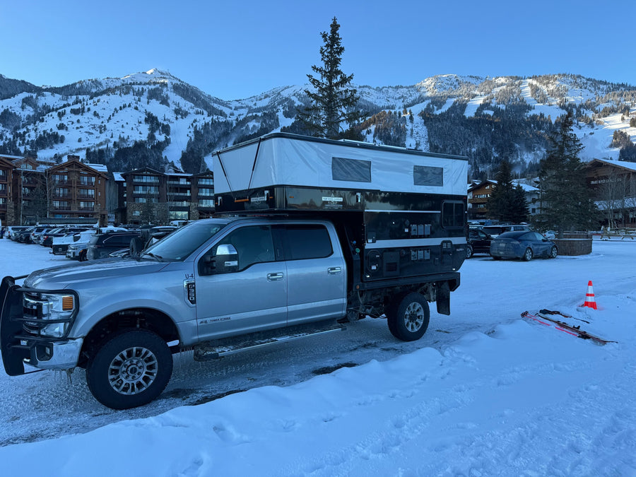 RV rental: Silver Ford F-250 with a Four Wheel Campers Hawk+ truck camper at a snowy ski resort. Mountains & lodge visible.