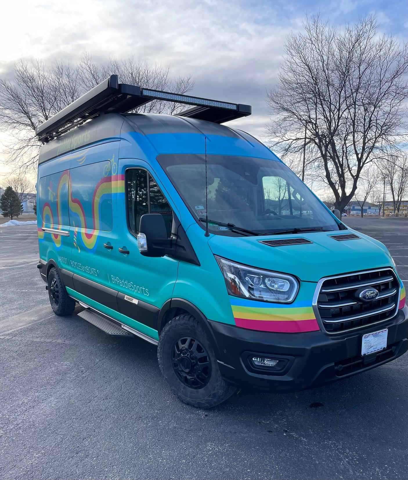 A vibrant, custom Ford Transit van, branded for paddle sports and bicycles, showcasing an RV rental option for outdoor adventures.