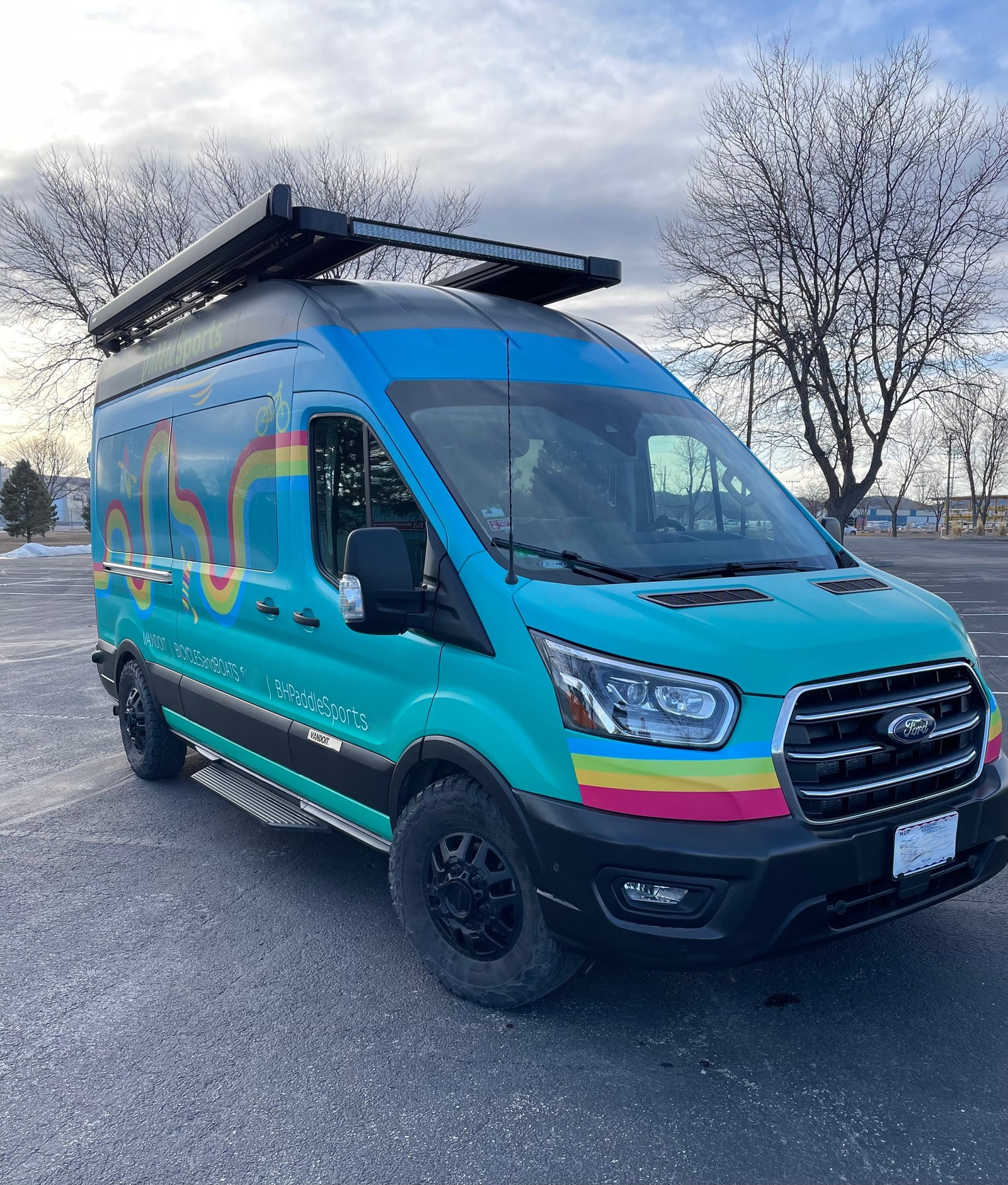 A vibrant, custom Ford Transit van, branded for paddle sports and bicycles, showcasing an RV rental option for outdoor adventures.