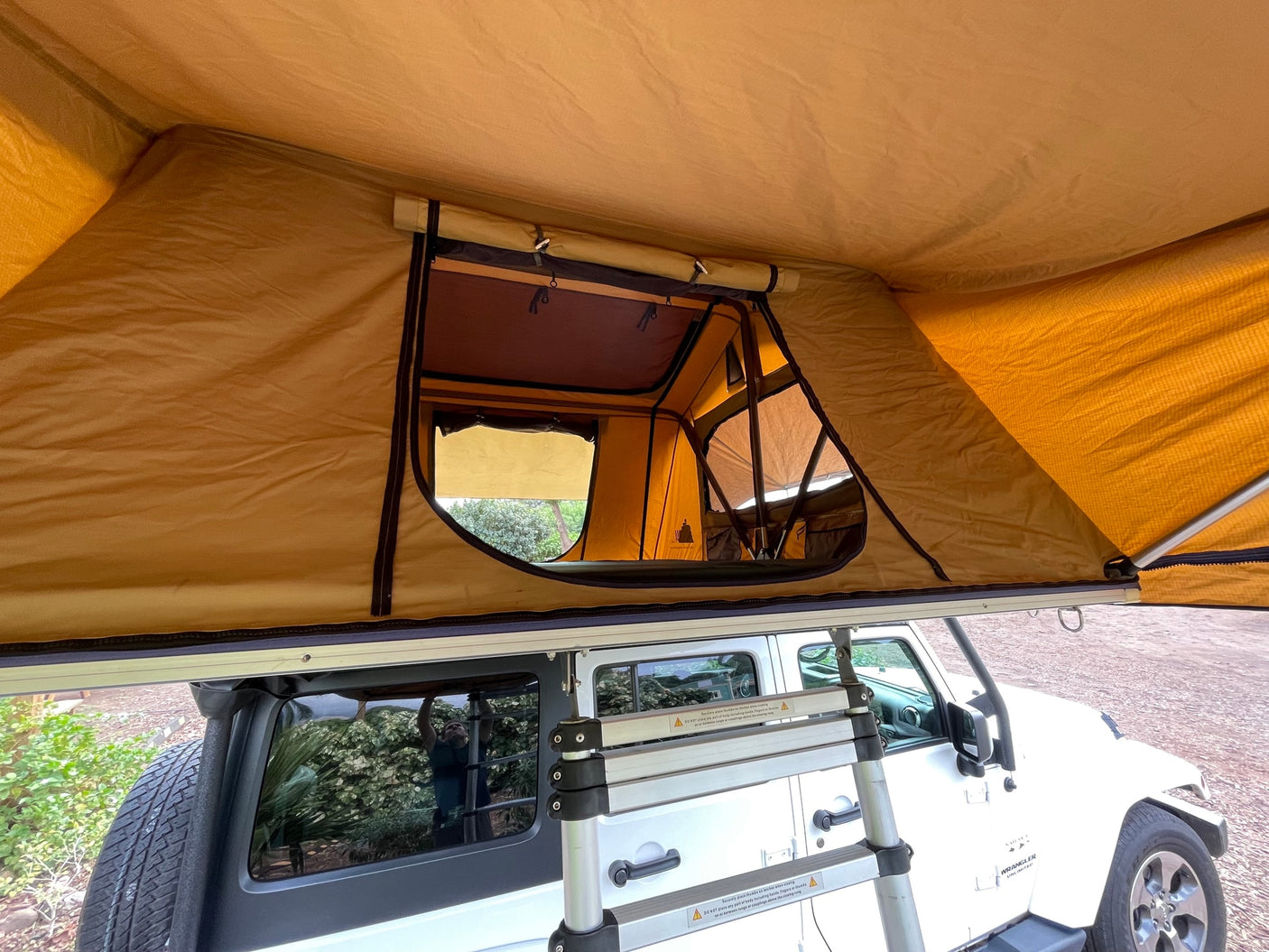 View from below an open rooftop tent on a white Jeep Wrangler, an agile RV rental alternative for overland camping adventures.