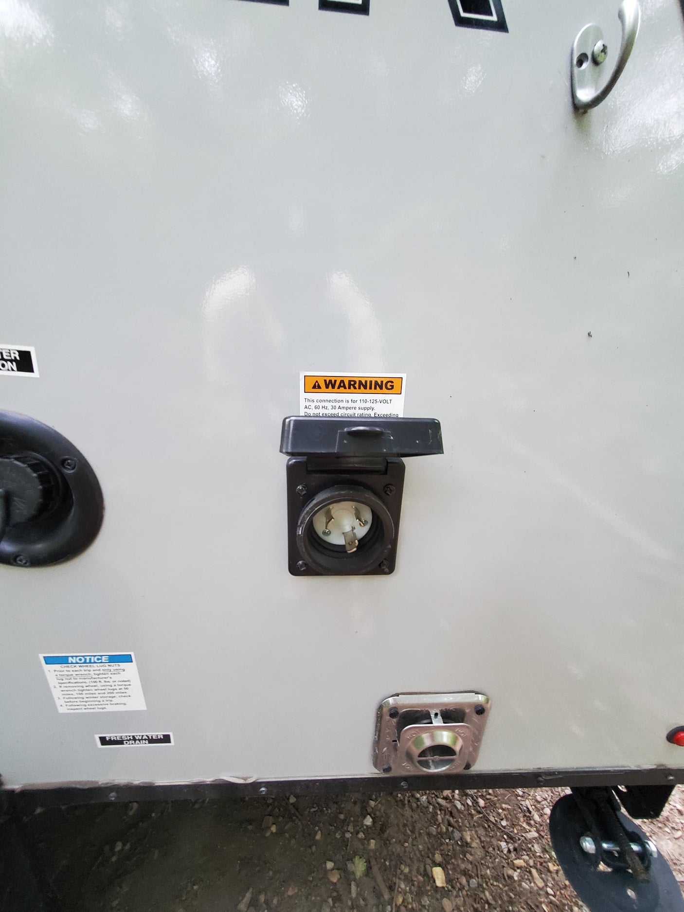 RV rental exterior: A 30 Amp shore power inlet, fresh water fill/drain, outdoor shower port, and various safety labels.