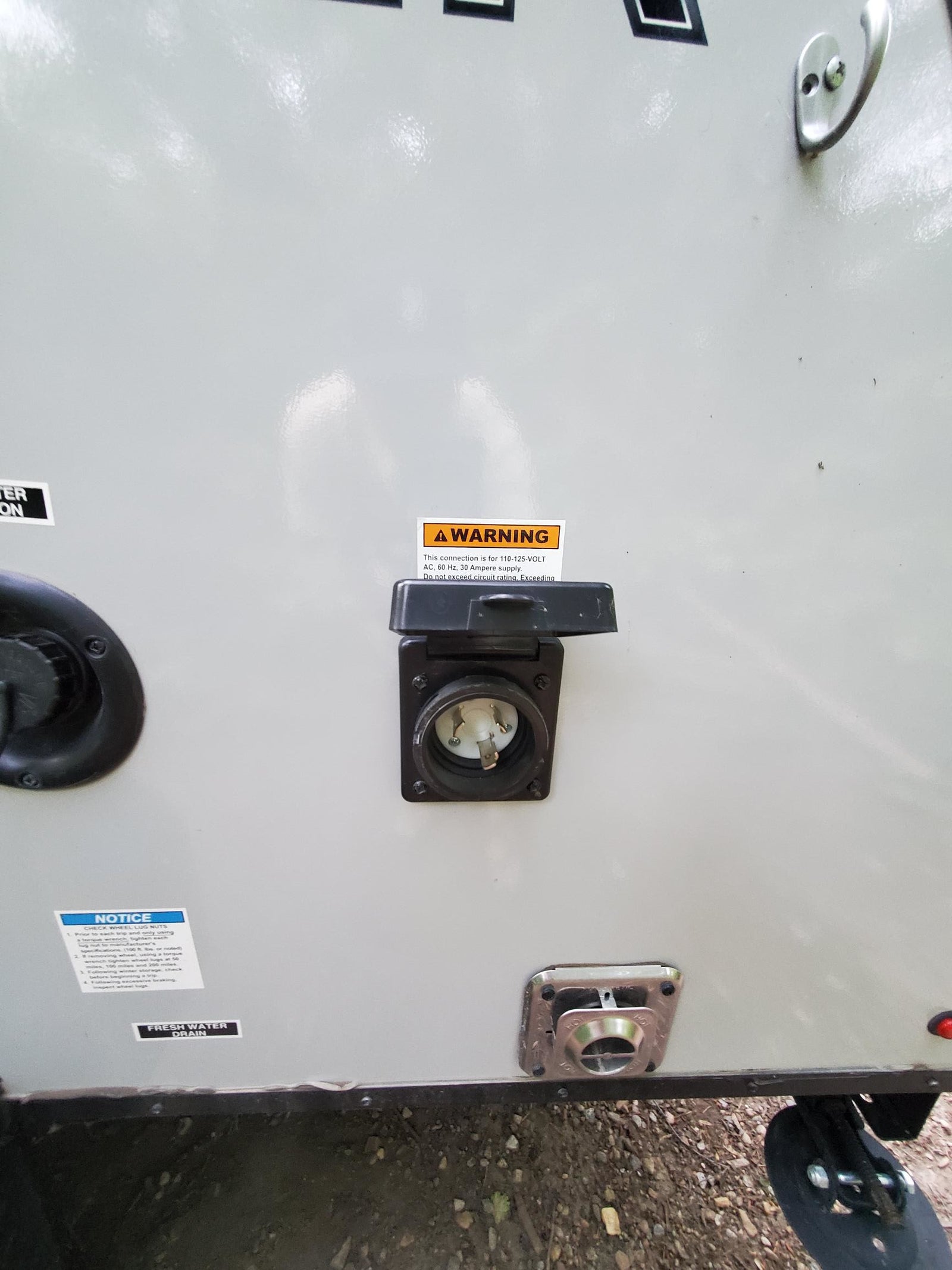 RV rental exterior: A 30 Amp shore power inlet, fresh water fill/drain, outdoor shower port, and various safety labels.