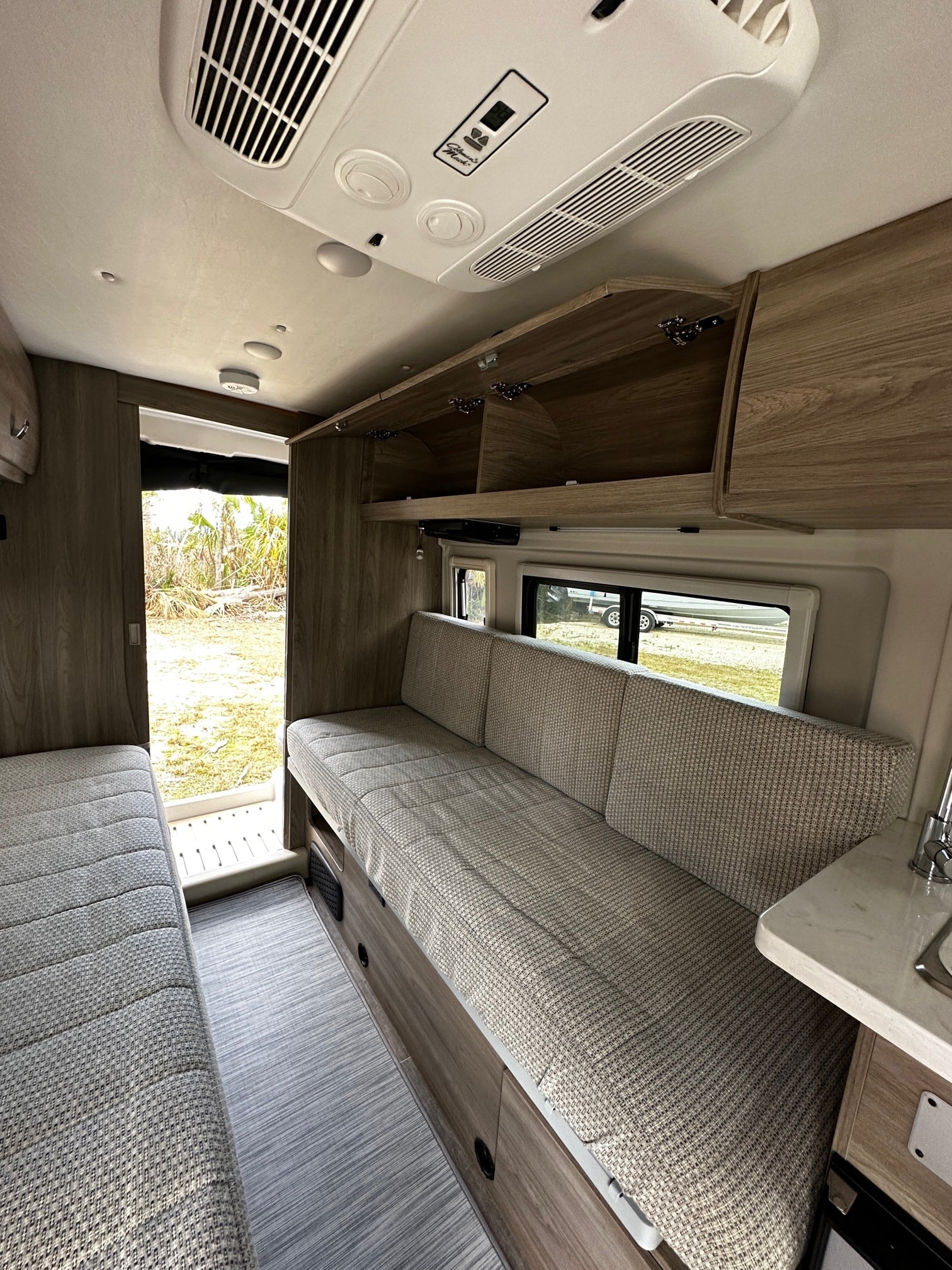 Bright RV rental interior with light wood cabinetry, a large sofa seating area, and a white AC unit on the ceiling.
