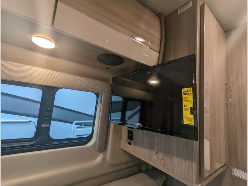 RV rental interior featuring a mounted flat-screen TV, modern overhead cabinets, and a window with blinds.