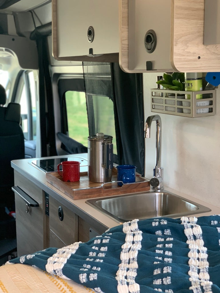 Inside a modern RV rental, featuring a compact kitchen with sink, cooktop, and coffee essentials on a wooden tray.
