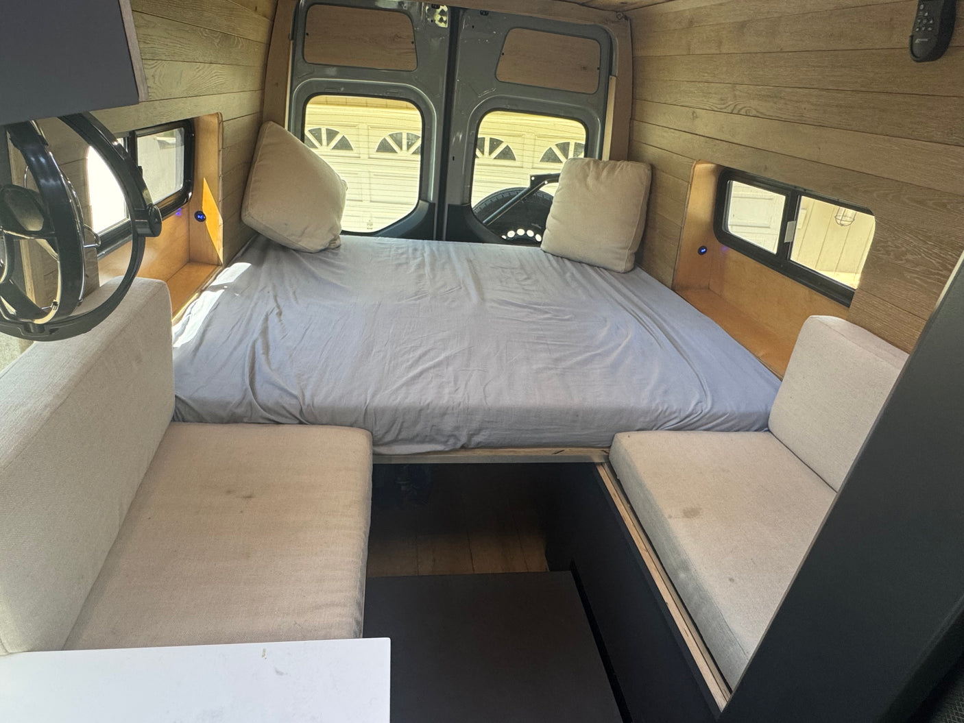 RV rental interior featuring a large bed, cozy bench seating, and warm wood finishes. Ideal for van life adventures.