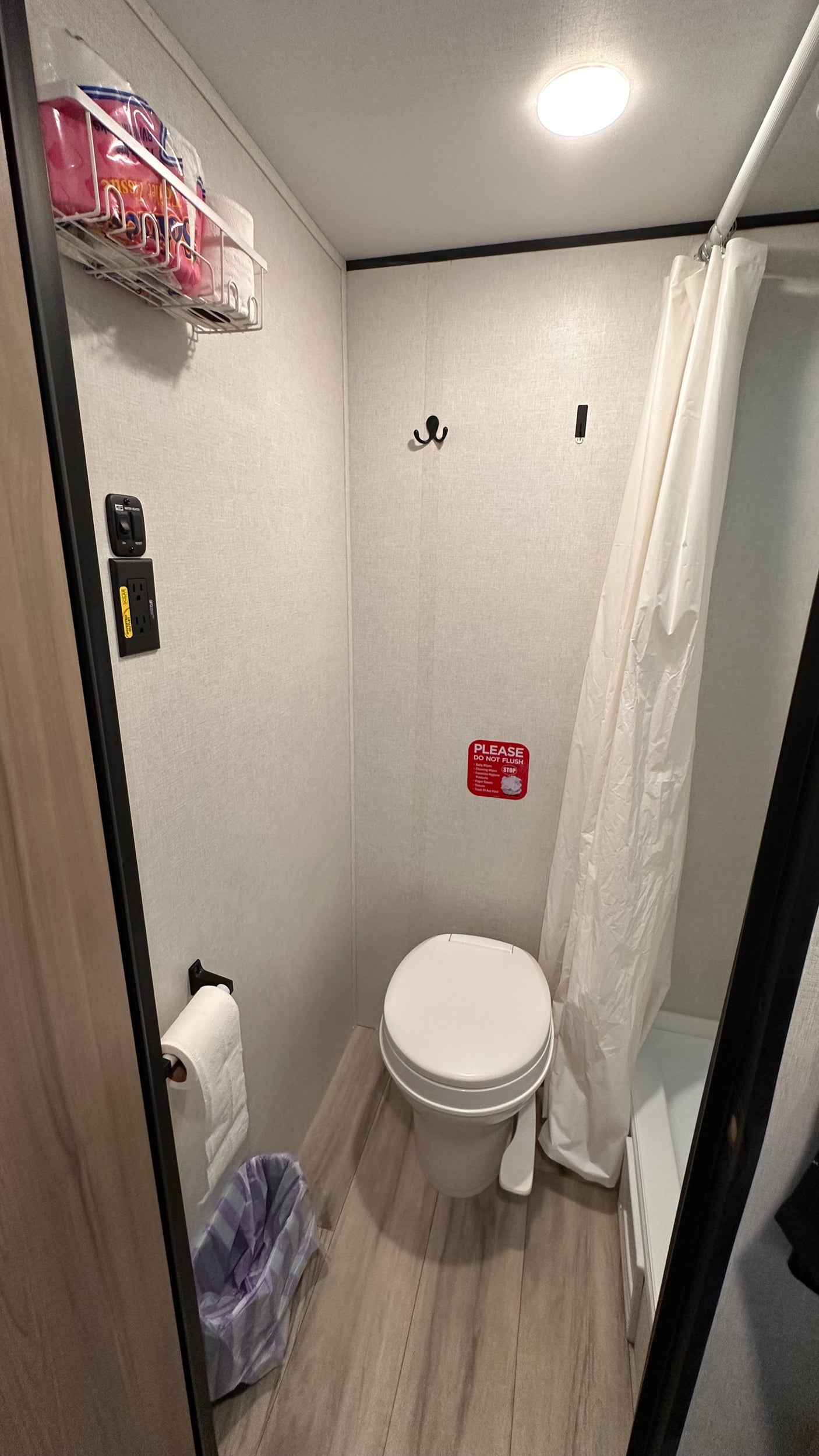This RV rental bathroom features a toilet, shower, wall-mounted storage, light switches, and a waste bin.