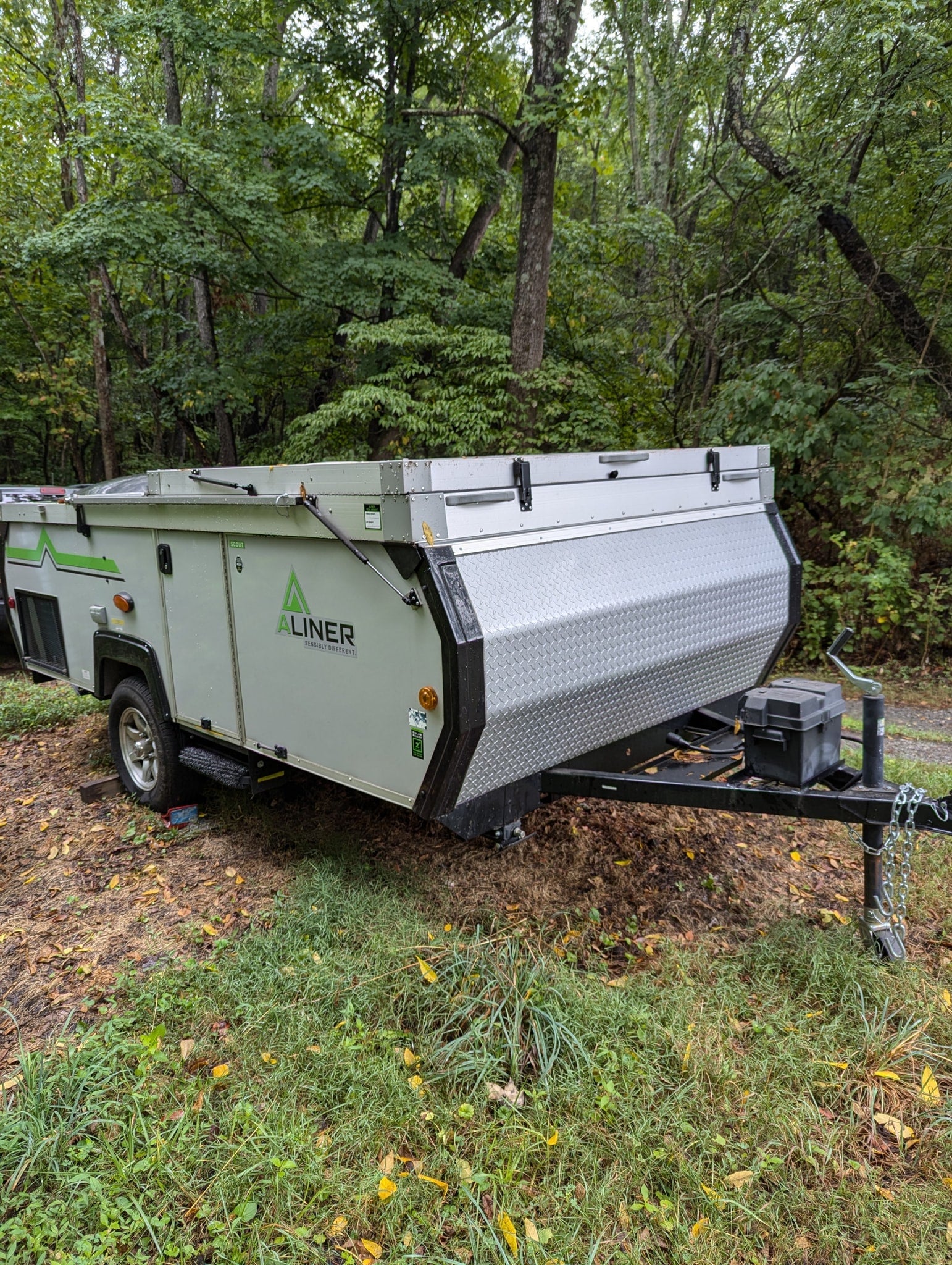 An Aliner pop-up camper, perfect for an RV rental, is parked at a wooded campsite, ready for adventure.