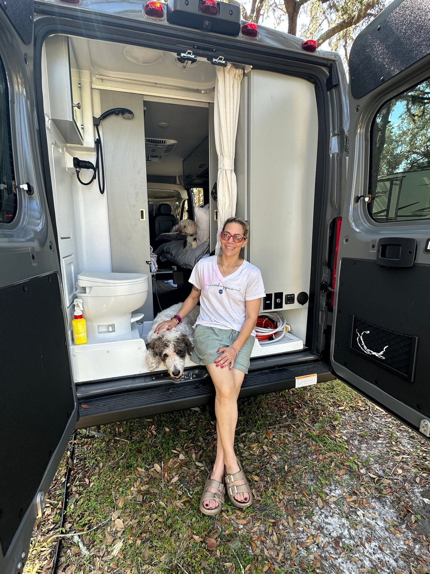 Enjoying the freedom of an RV rental! Woman & dog relax at the back of their camper van. Toilet & shower visible.