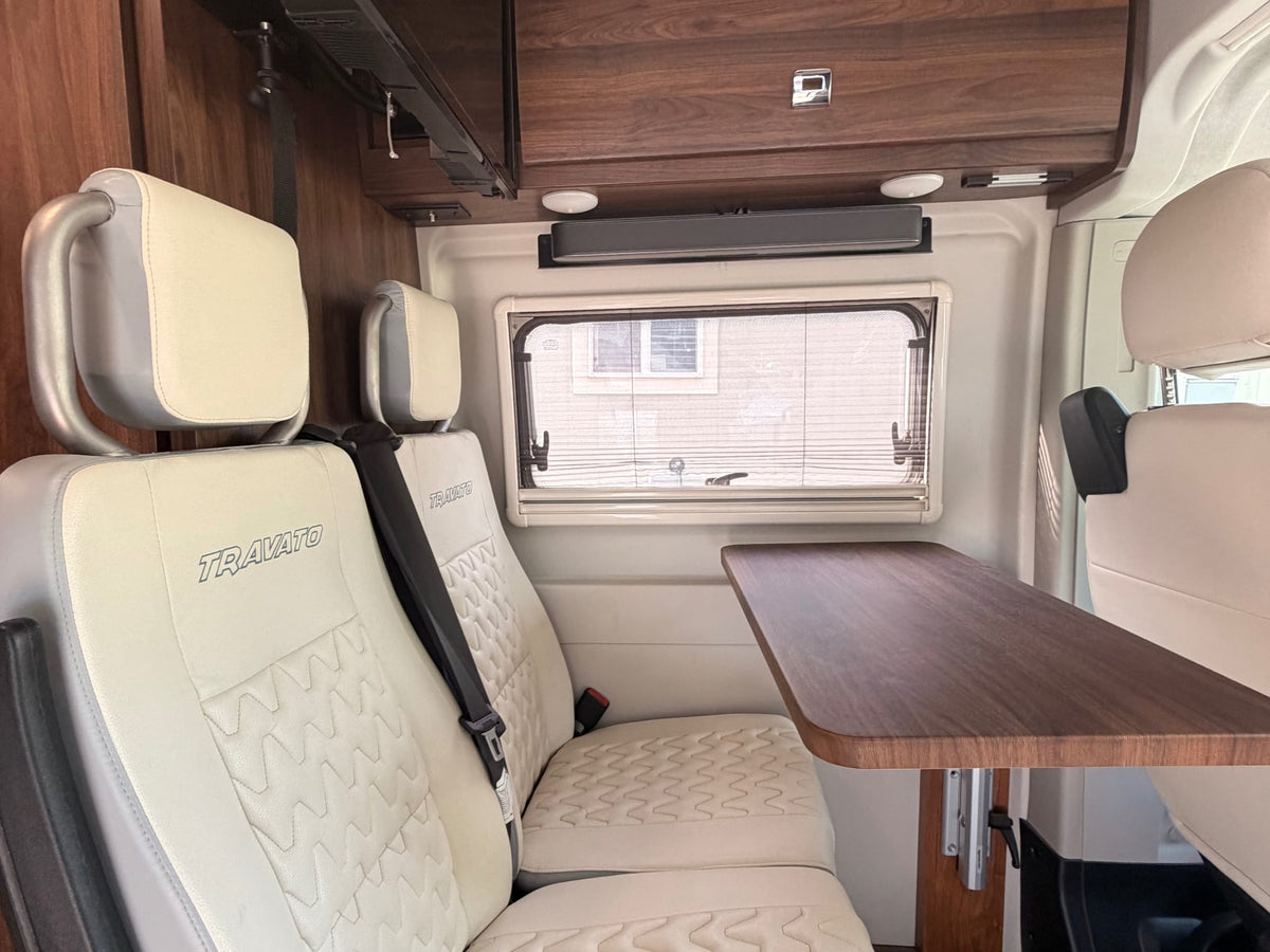 plugged in and parked on dirt. Features a ladder & bike rack on the rear.|This RV rental features a comfortable dinette: light "TRAVATO" seats — photo 2
