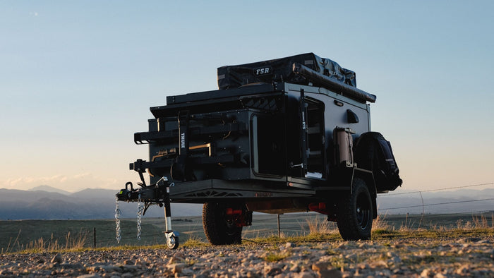 ideal for RV rental adventures. Features roof-top tent & propane for camping.|A rugged black overlanding trailer with a rooftop tent and gear