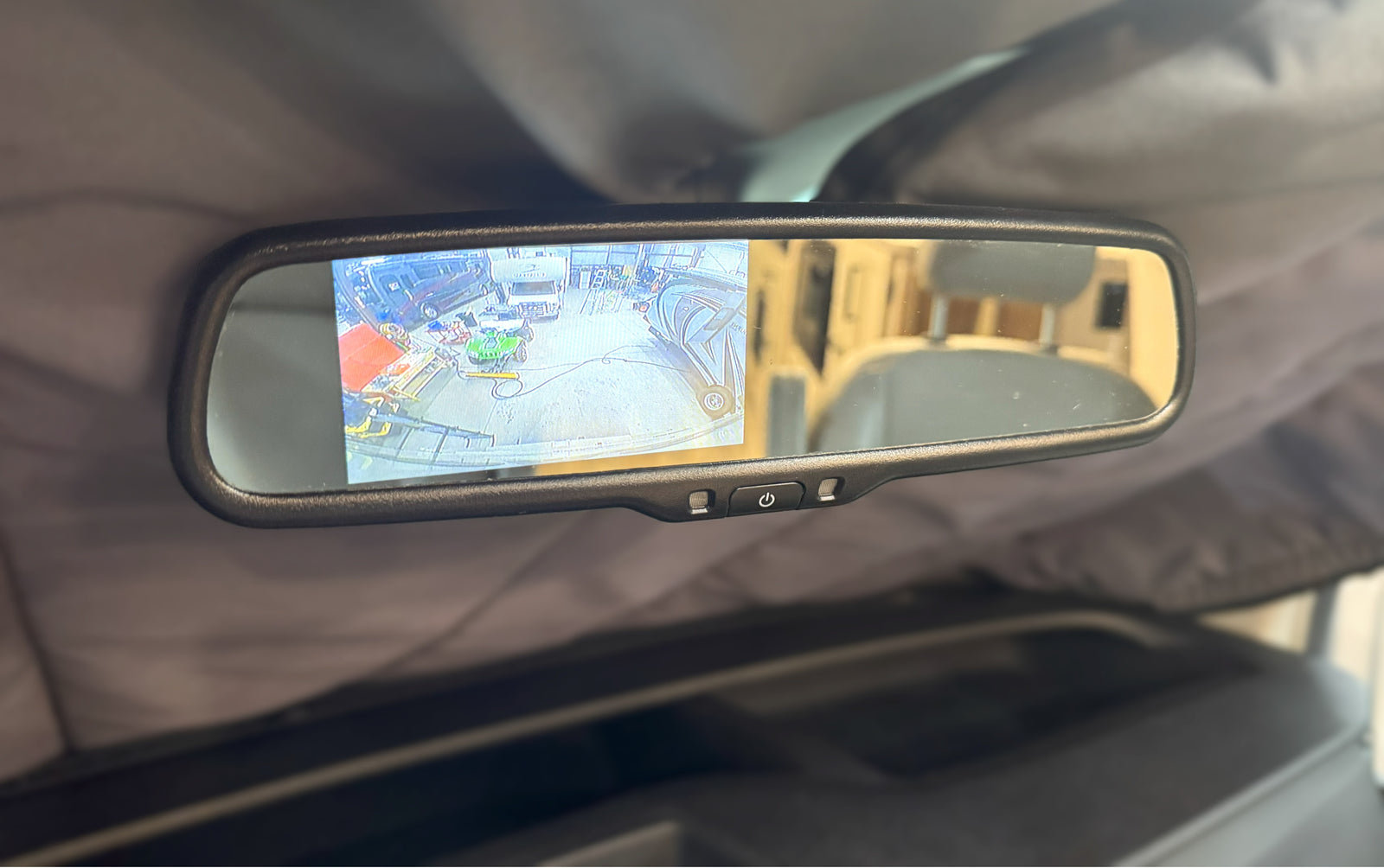 Inside an RV rental, a rearview mirror displays a backup camera view of a garage with a van, ATV, and boat.