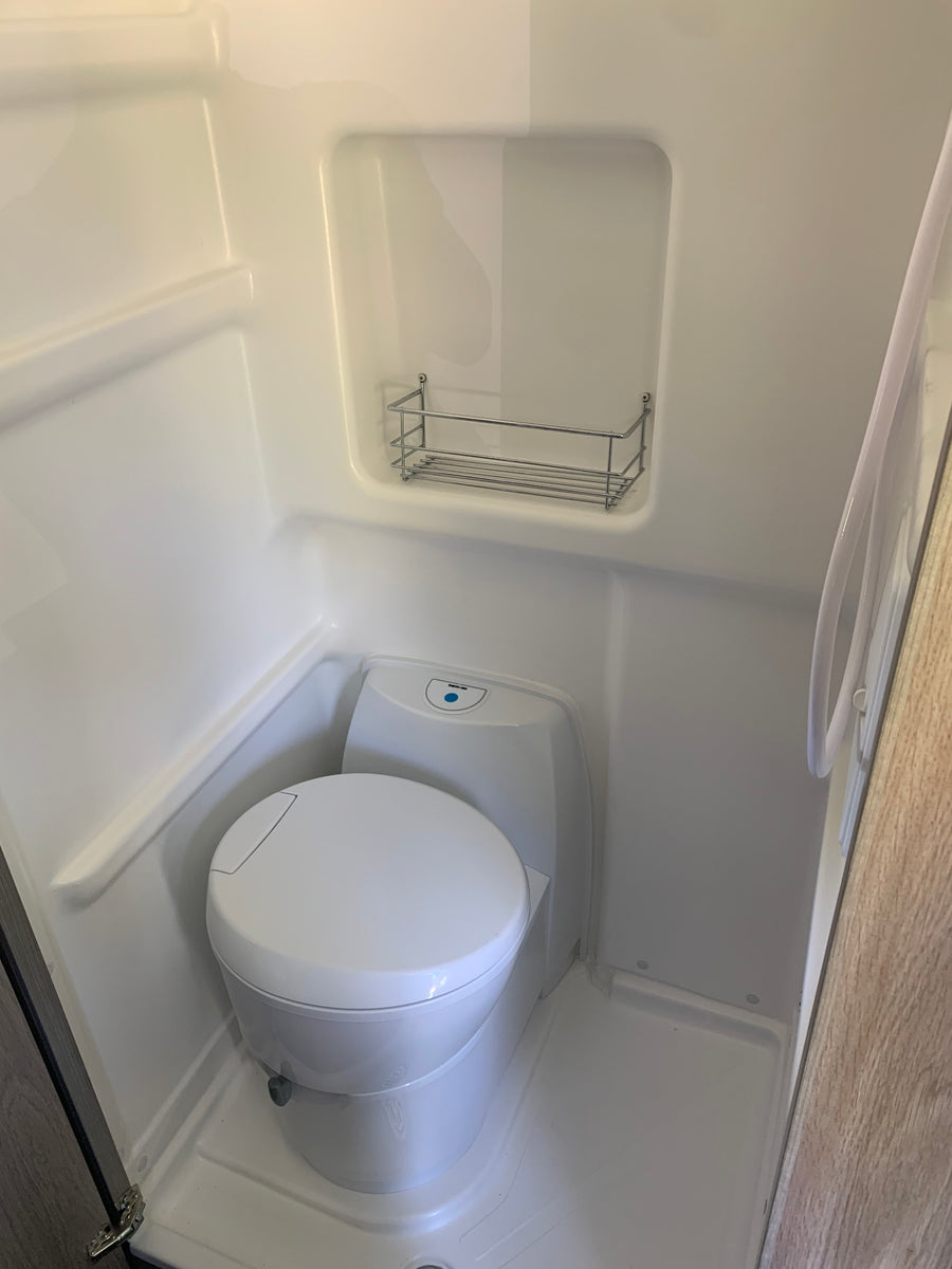 This RV rental features a compact wet bath with a toilet, shower hose, and handy storage rack for toiletries.
