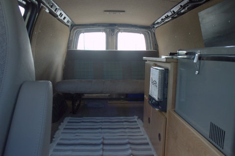 Inside a cozy RV rental: a modern camper van conversion featuring a bench seat, portable fridge, and heater for travel. — photo 7