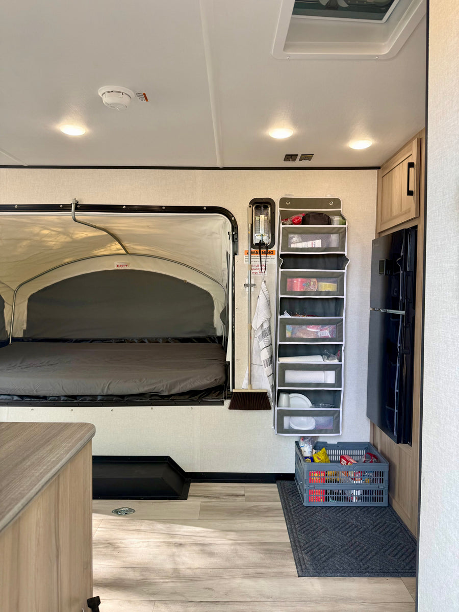 RV rental interior: A compact living space with a pop-out bed, vertical storage organizer, and refrigerator.