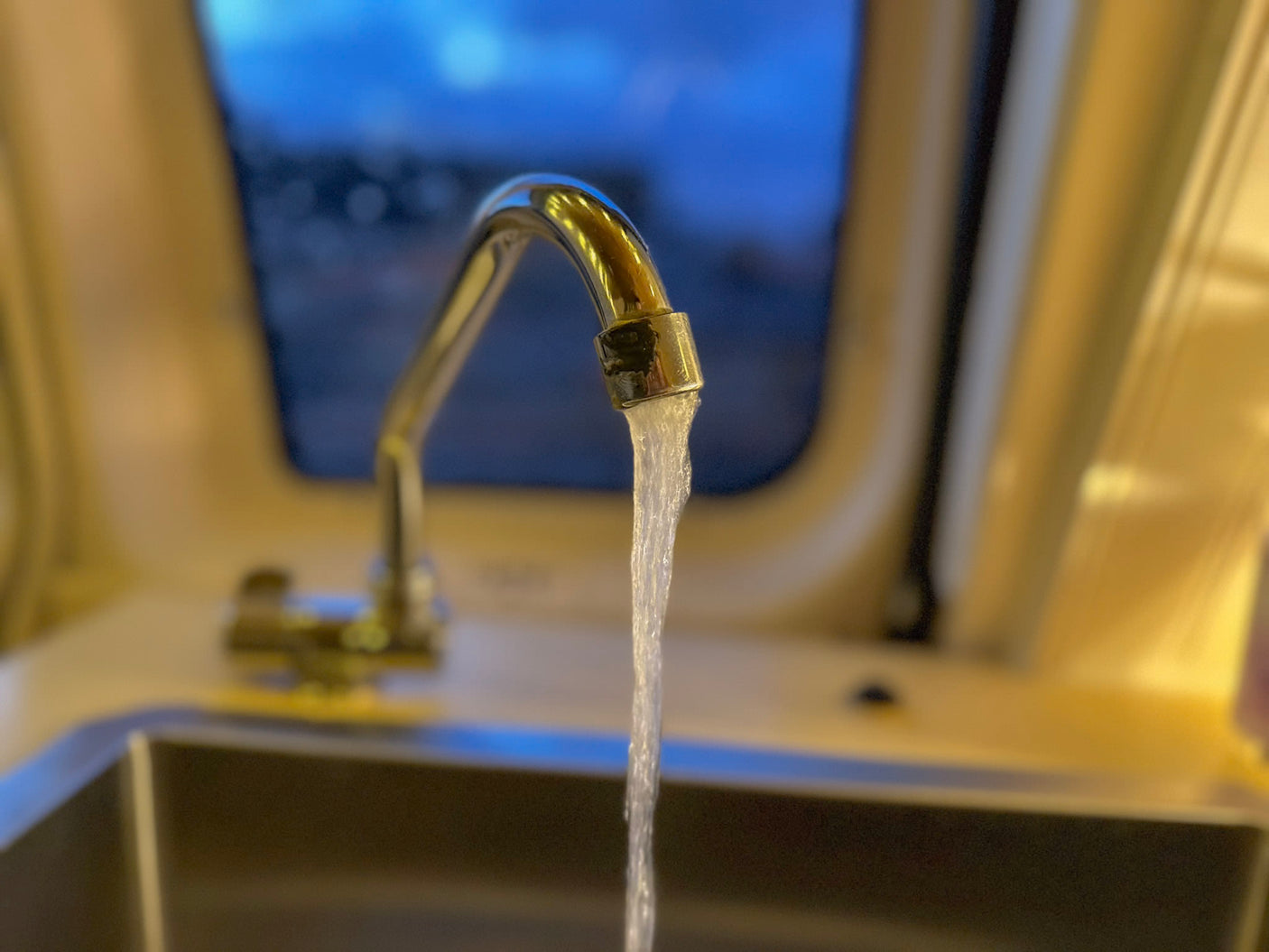 RV rental: Water flows from a shiny faucet into a sink in this compact kitchen. Blue window view.