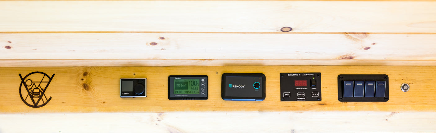 This RV rental features integrated controls: Webasto heater, Renogy battery, SeeLevel tank monitor, and other switches on wood.