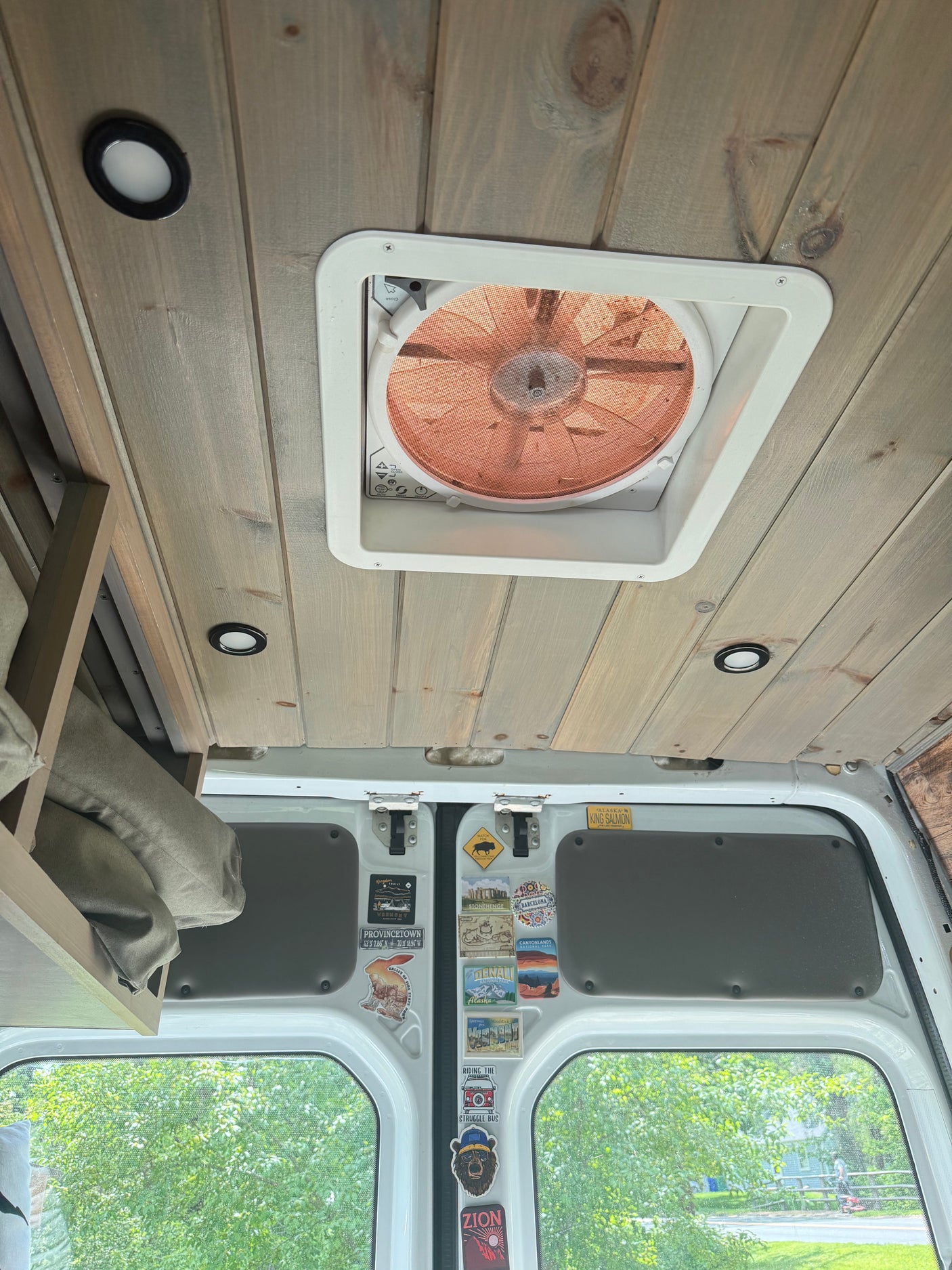 This cozy rv rental interior features a wood-paneled ceiling, a roof fan, LED lights, and travel stickers on the back windows.
