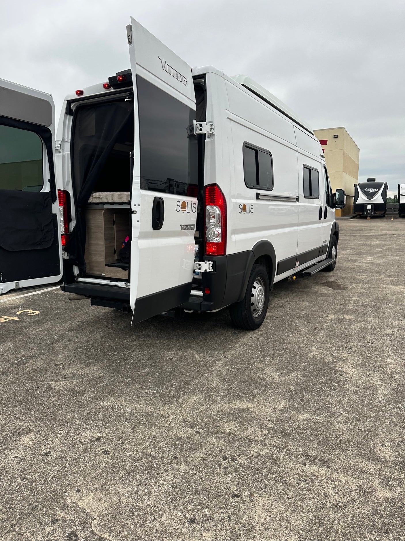White Winnebago Solis camper van with open rear doors showing interior. Ideal RV rental for travel adventures.