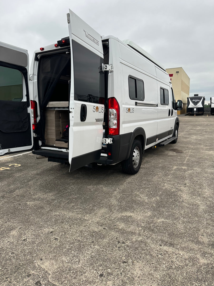 White Winnebago Solis camper van with open rear doors showing interior. Ideal RV rental for travel adventures.