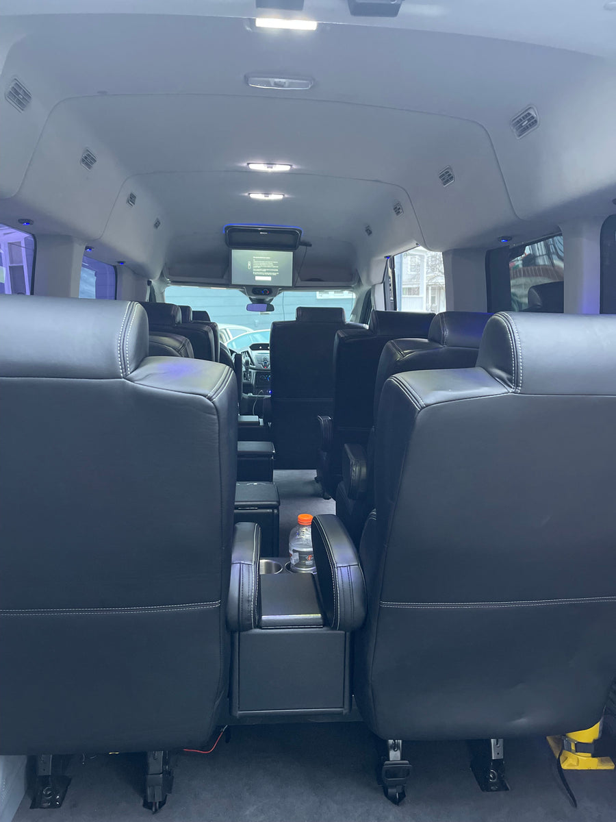 Comfortable interior of a passenger van, ideal for RV rental. Features plush black leather seats, overhead screen, and ample lighting.