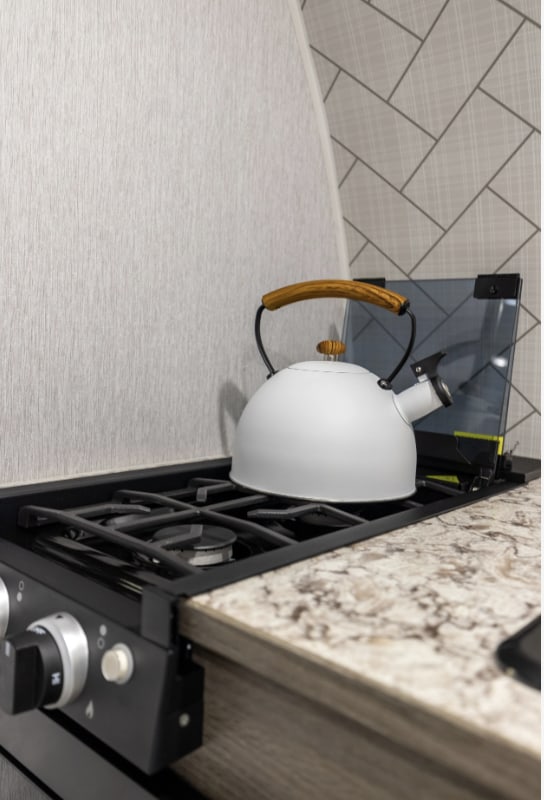 Cozy RV rental kitchen featuring a white kettle on a compact gas stove. Ideal for your next road trip!
