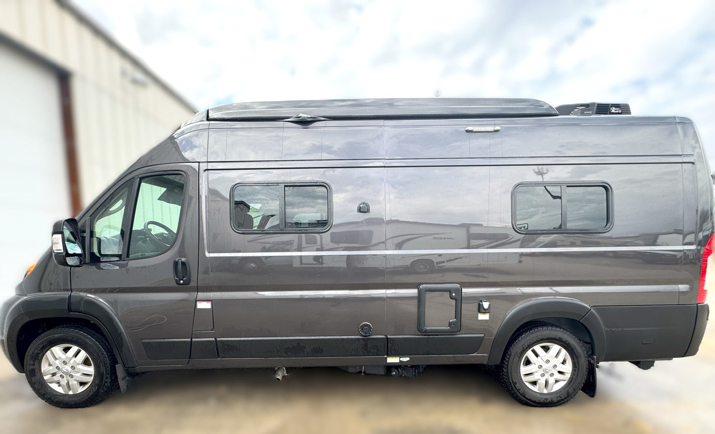 Side view of a sleek gray camper van, ideal for RV rental. Features include a raised roof, side windows, and a rooftop AC unit.