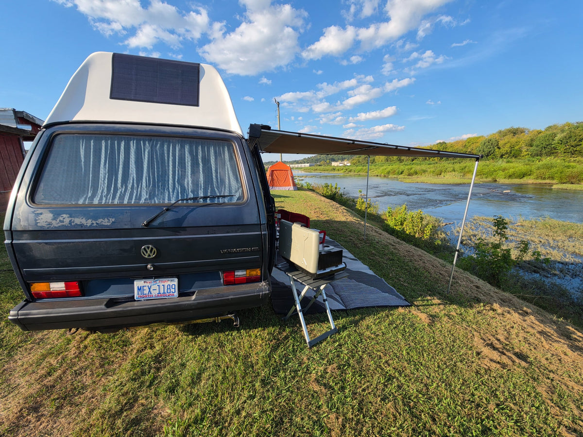charging by a scenic river campsite.|Enjoying an RV rental by the river: a blue camper van with an awning — photo 7