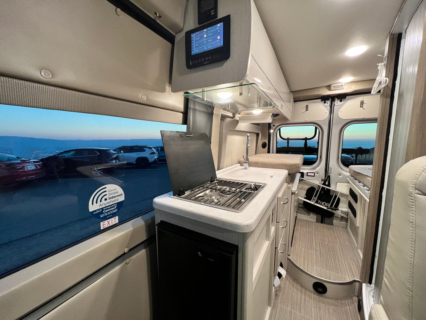 Interior of an rv rental, featuring a modern kitchenette, control panel, and an outside view from the window.