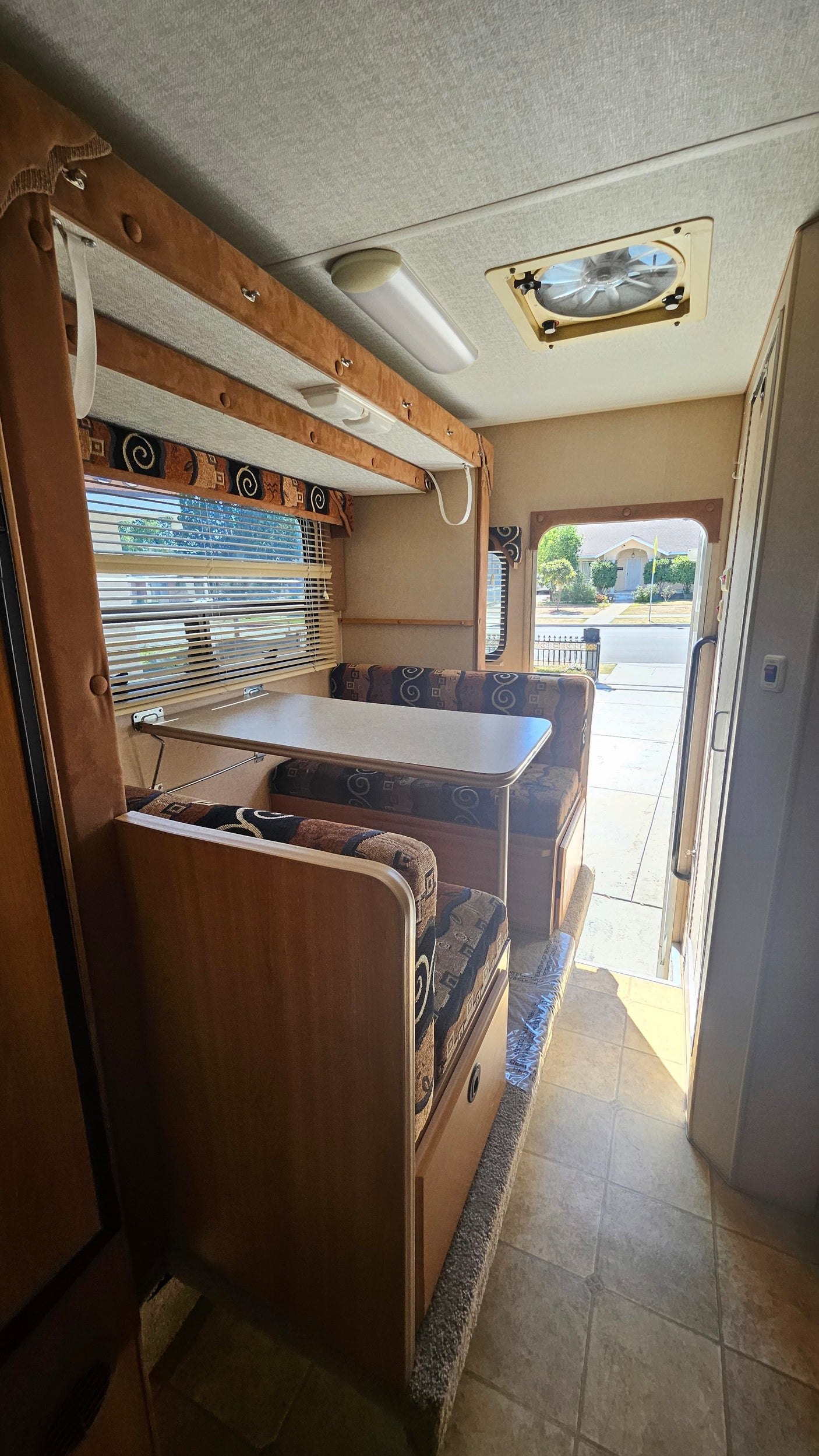 Explore this RV rental's interior: a cozy dinette with patterned cushions, a large window with blinds, and practical tile flooring.