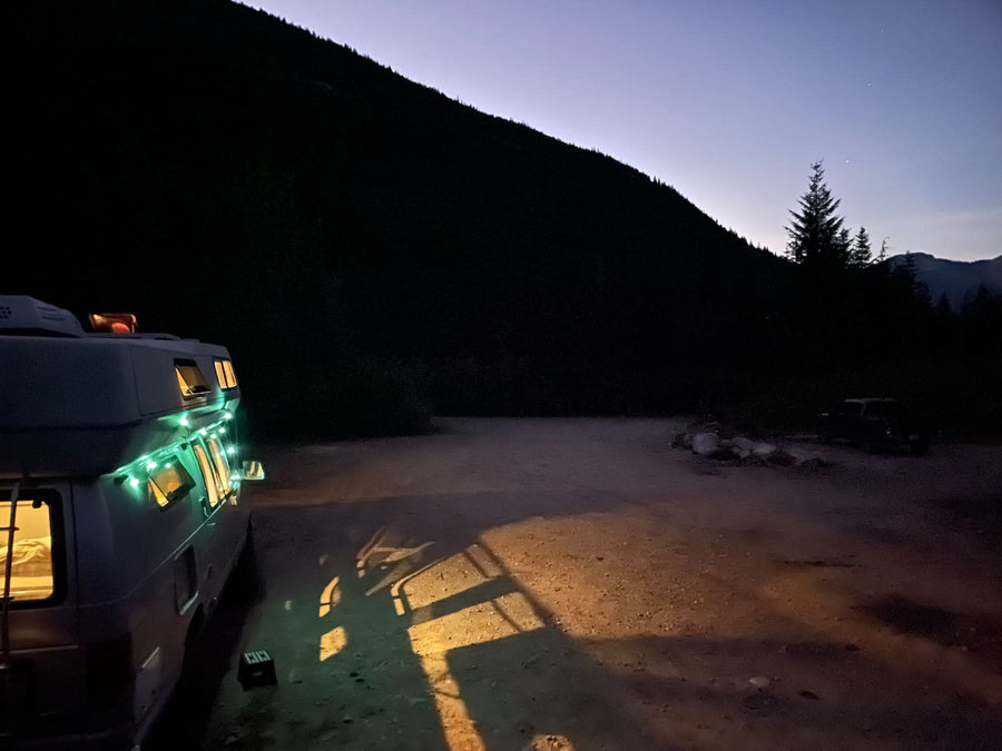 RV rental brightly lit, parked for night camping in a vast mountain landscape at twilight.