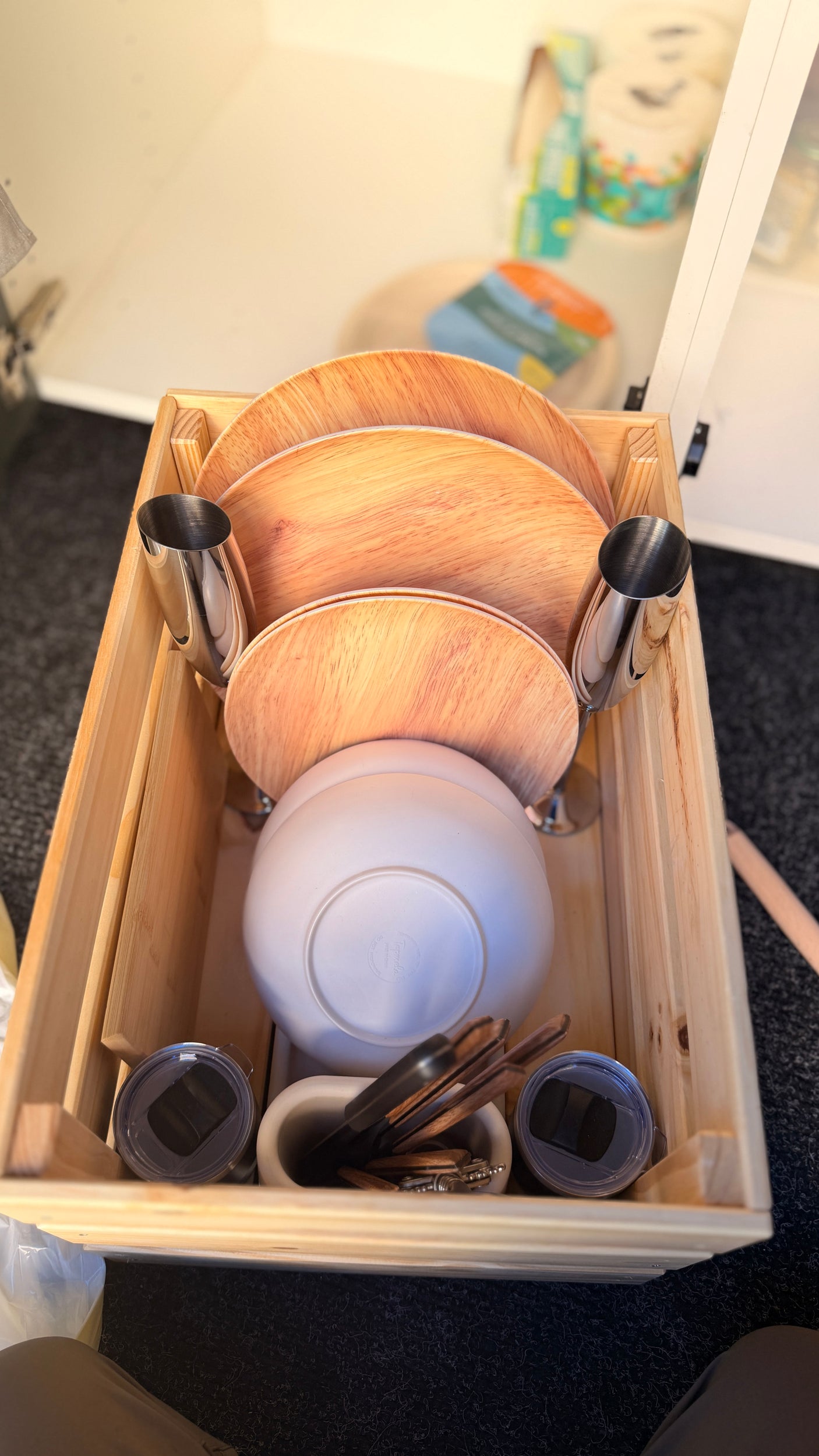 RV rental kitchen essentials: stacked plates, bowls, cups, and utensils neatly organized in a wooden box for travel.