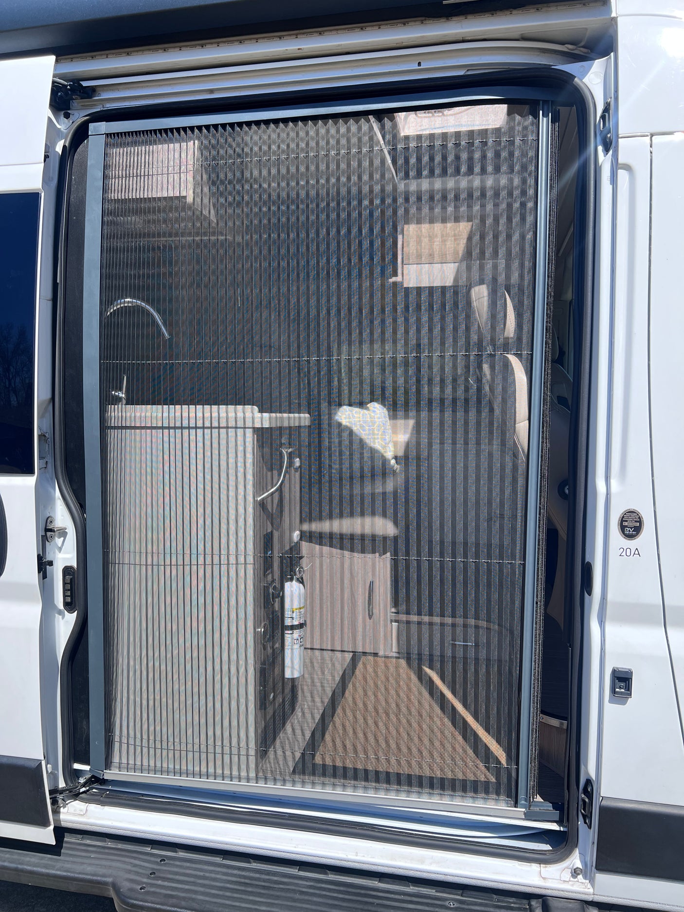 RV rental's open side door with a pleated screen, revealing an interior sink and fire extinguisher inside the camper van.