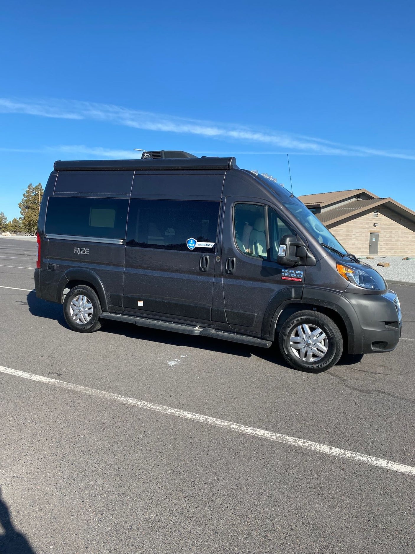 Dark grey Ram ProMaster RV rental parked outdoors under a clear blue sky. Ready for your next adventure.
