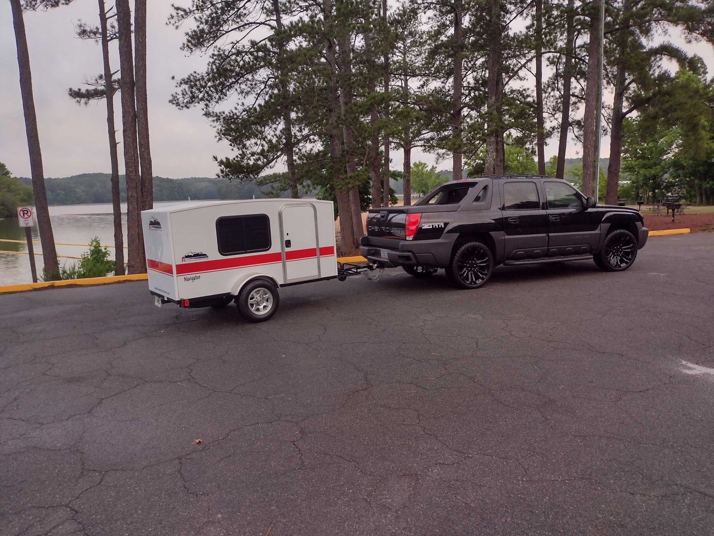 Experience nature with this RV rental: a black truck towing a compact white Runaway teardrop camper by a lake.