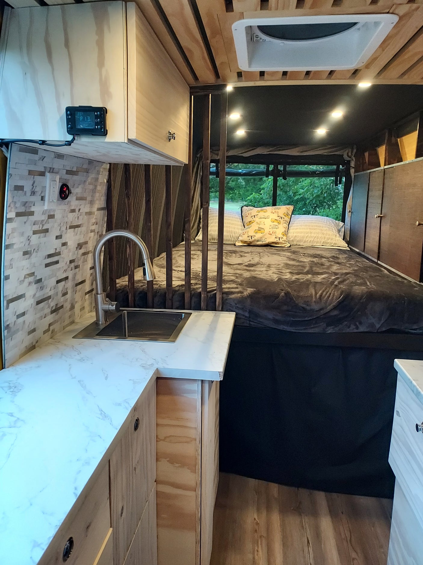 Cozy RV rental interior with a bed, compact kitchen with sink, wood paneling, string lights, and a window view.