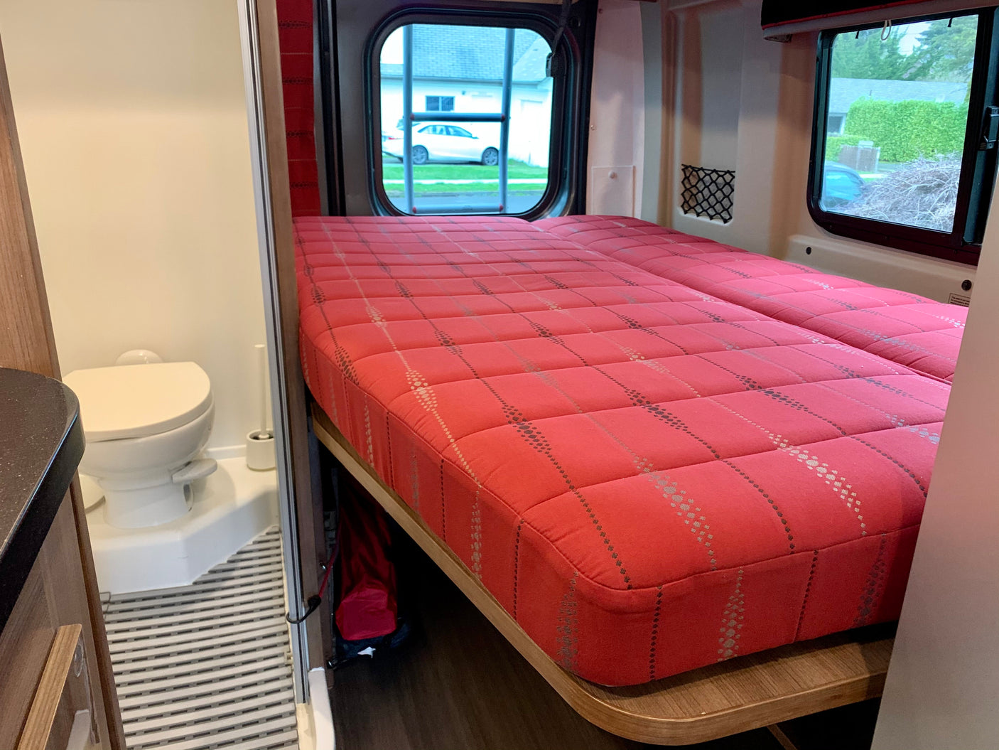 RV rental bedroom and bathroom. Features a large red bed, built-in toilet, and window views.