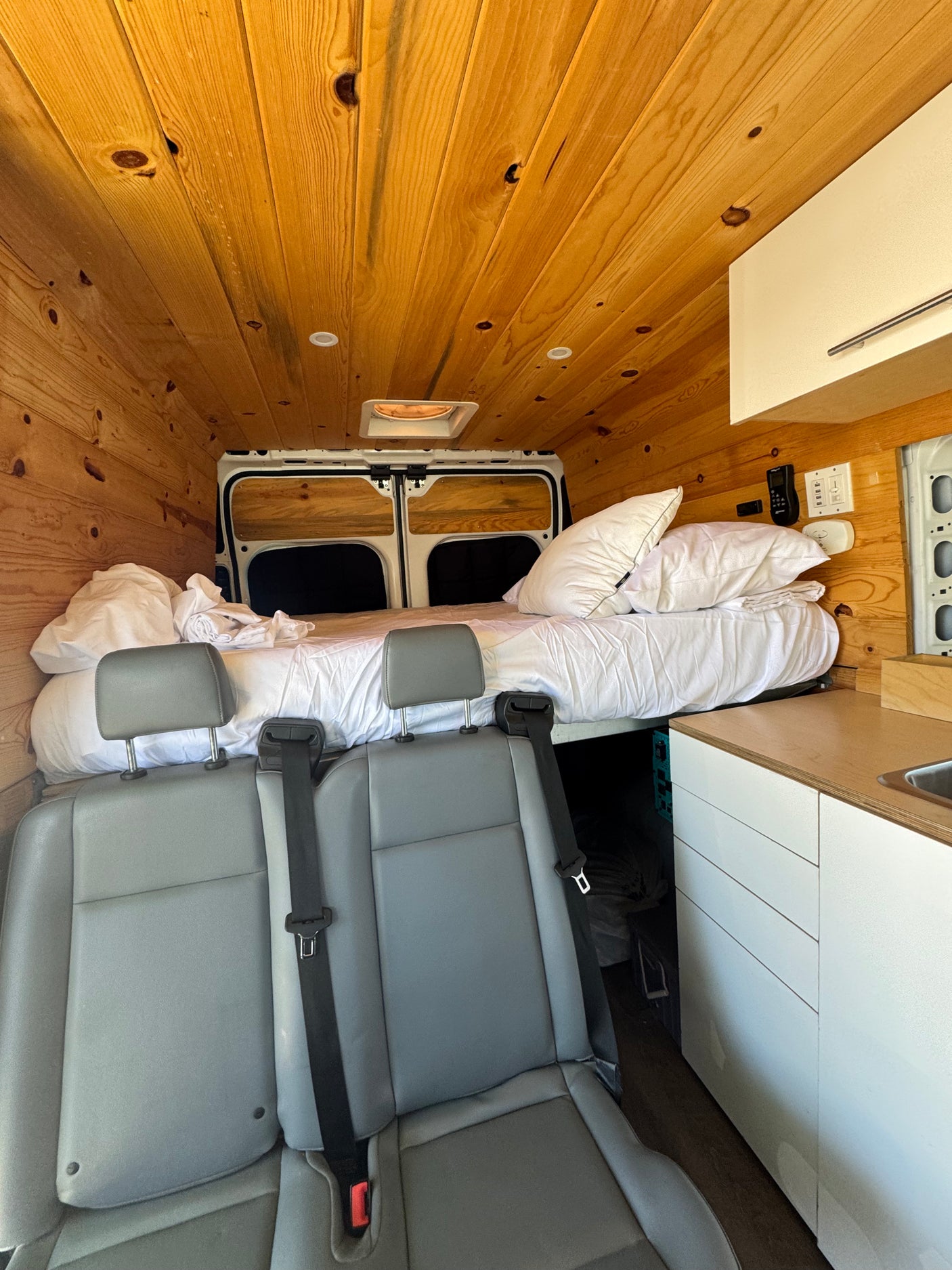 Interior of a cozy RV rental: wood-paneled walls, bed, kitchenette, and passenger seats.
