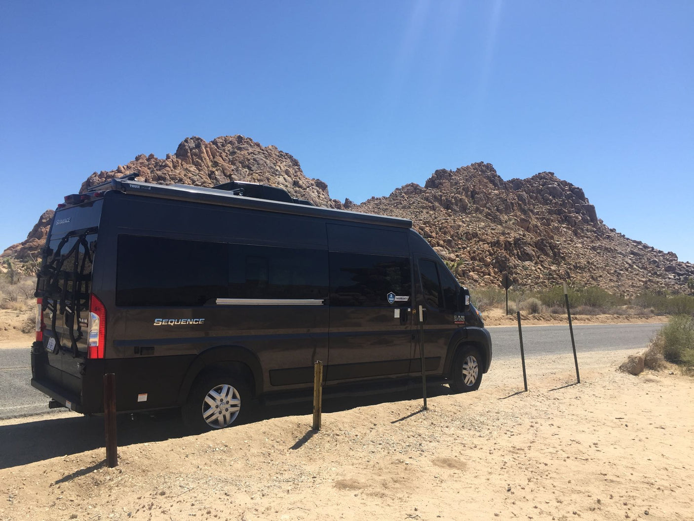 Dark Sequence RV rental parked by rocky desert mountains under a clear sky. Perfect for a road trip!