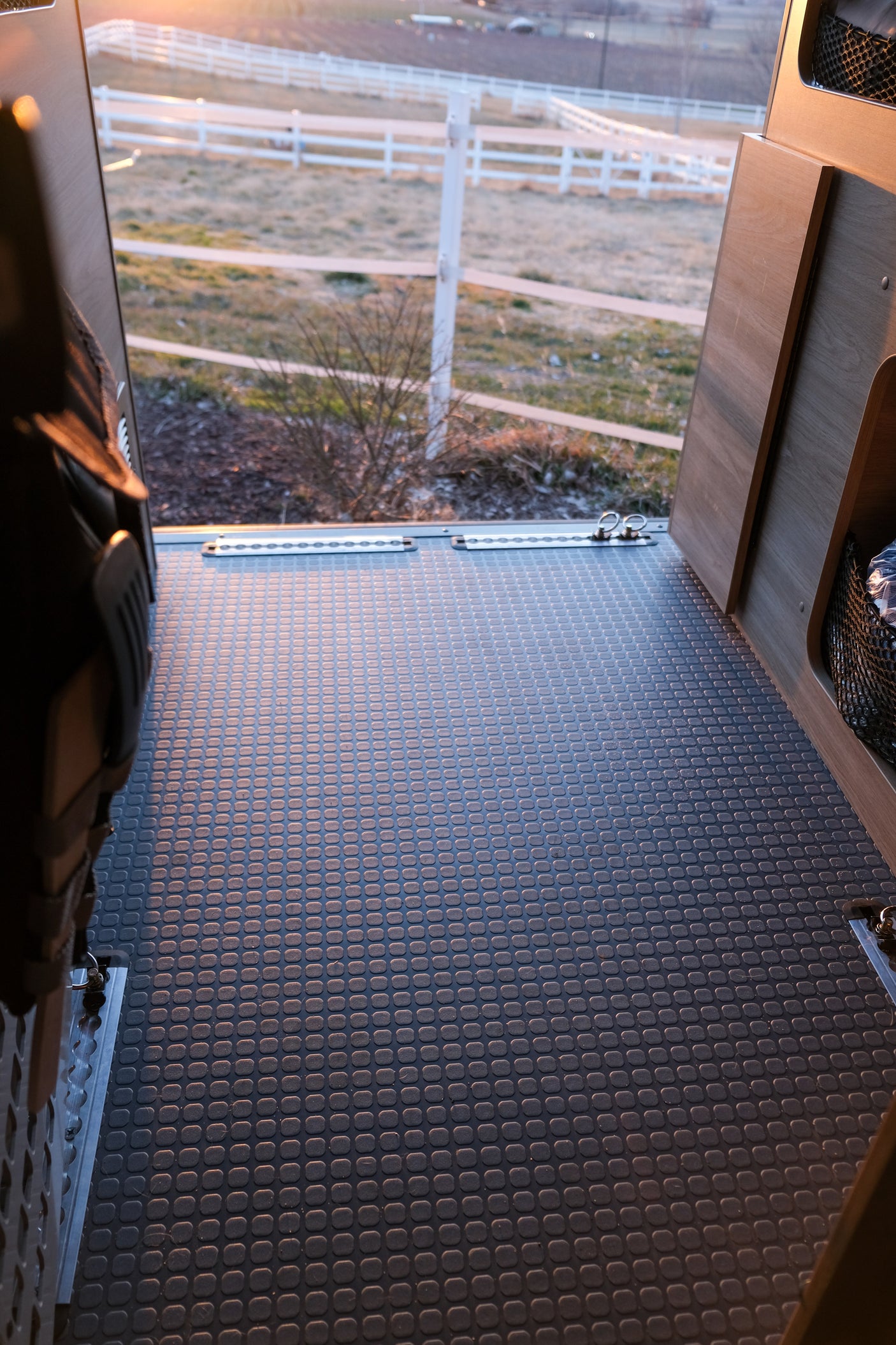 Spacious RV rental interior with textured floor, cargo tracks, and a scenic view of a fenced outdoor landscape.