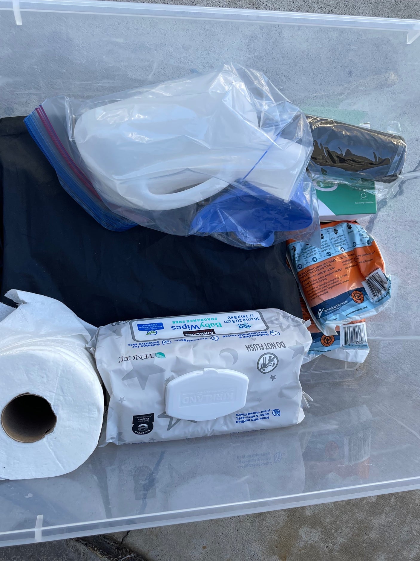 RV rental hygiene kit: Portable toilet, Kirkland wipes, toilet paper, and waste bags, all in a clear storage bin for camping.