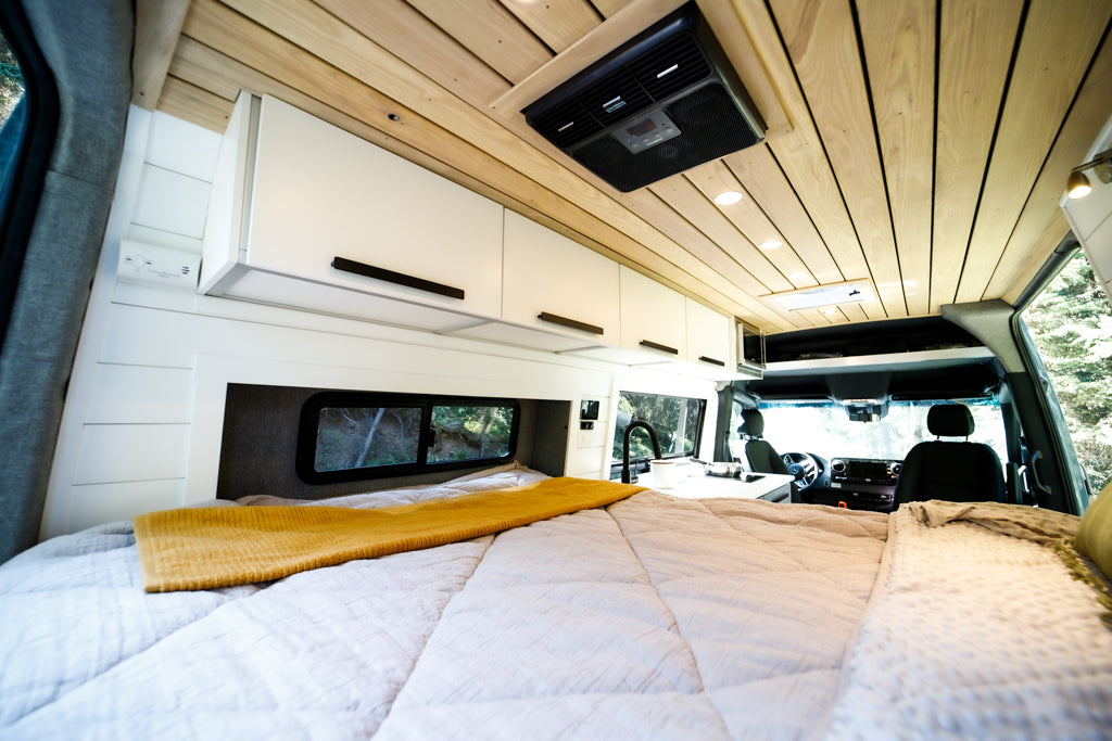 Explore this modern RV rental interior, featuring a large bed, sleek white cabinets, wood ceiling, and kitchenette.