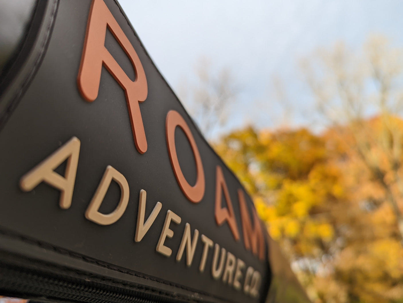 "ROAM ADVENTURE CO" branding on an RV or travel gear, with blurred autumn leaves. Ideal for an RV rental journey.